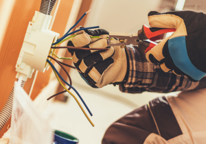 hands with electrical gloves using tool on electrical wiring in wall